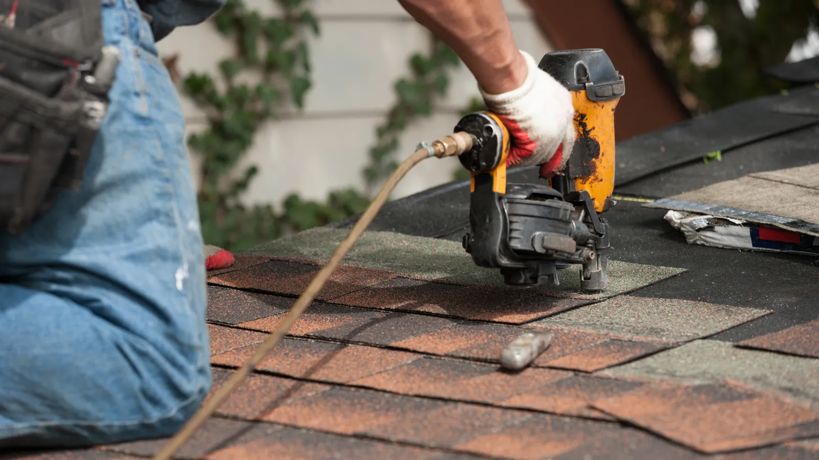 A gloved roofer nailing shingles with an air nailer